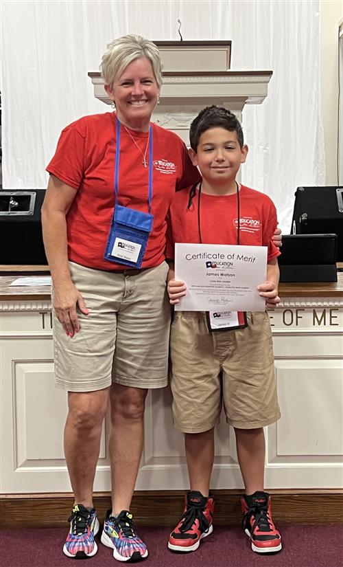 Woman and boy standing next to each other. The boy is holding a certificate.
